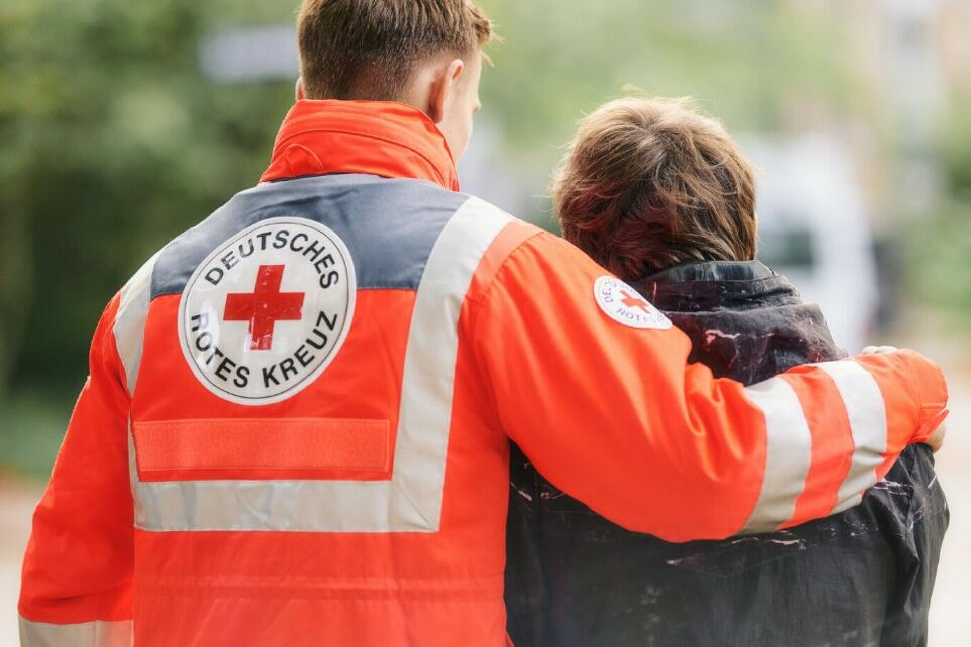 Mann in Rotkreuzjacke legt den Arm und eine Frau